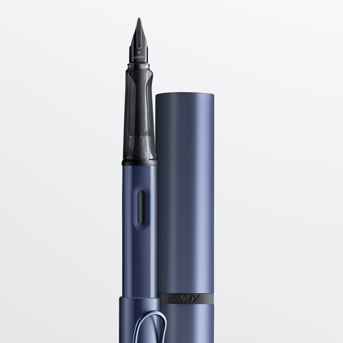 A close-up studio shot of a blue metallic fountain pen with its matching cap standing beside it on a clean white background. The nib and barrel are clearly visible, and the brand name 'LAMY' appears on the cap band and nib.