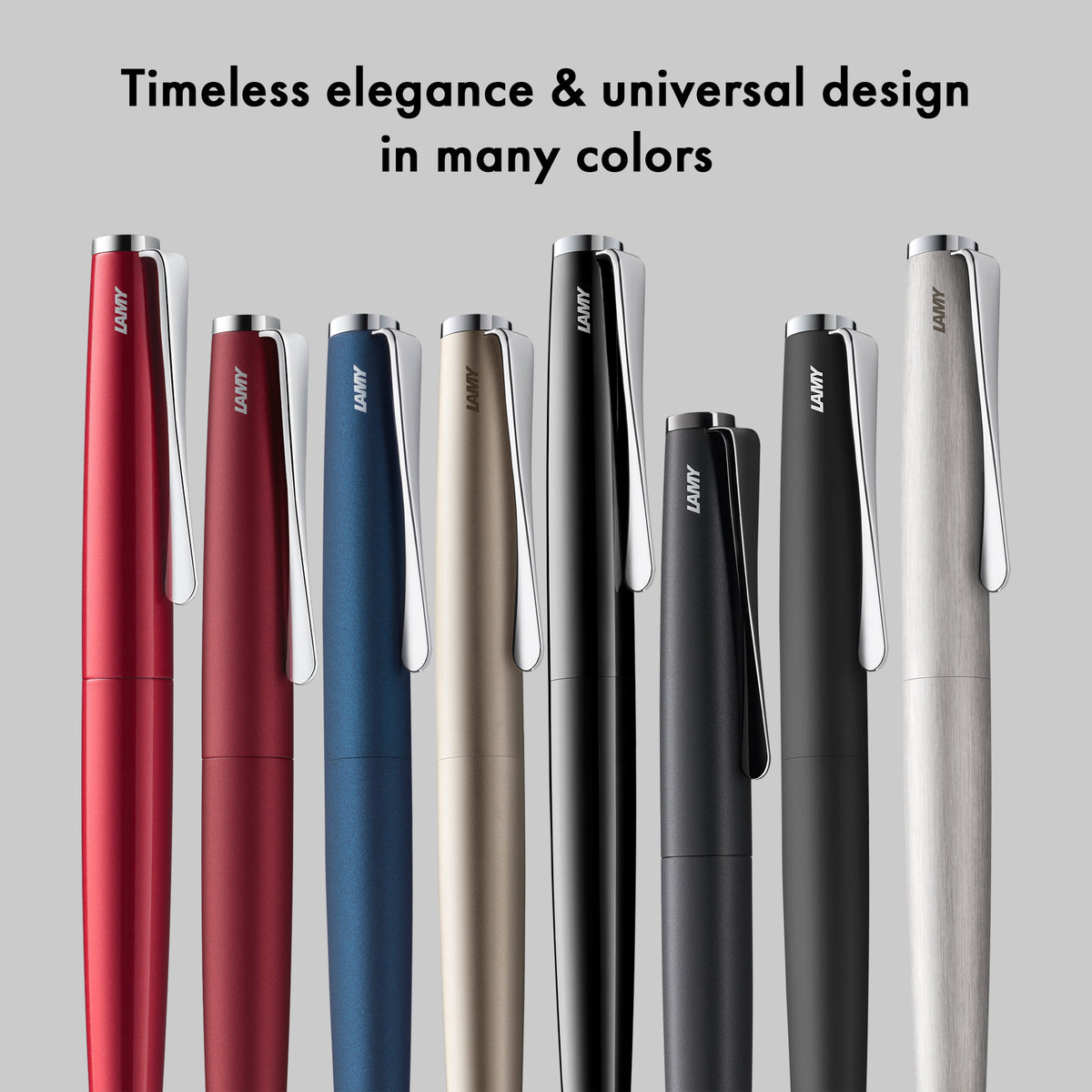 Seven LAMY pens in different colors are lined up against a light gray background with the text 'Timeless elegance & universal design in many colors' at the top. The pens include red, burgundy, blue, champagne beige, black, dark gray, and silver.